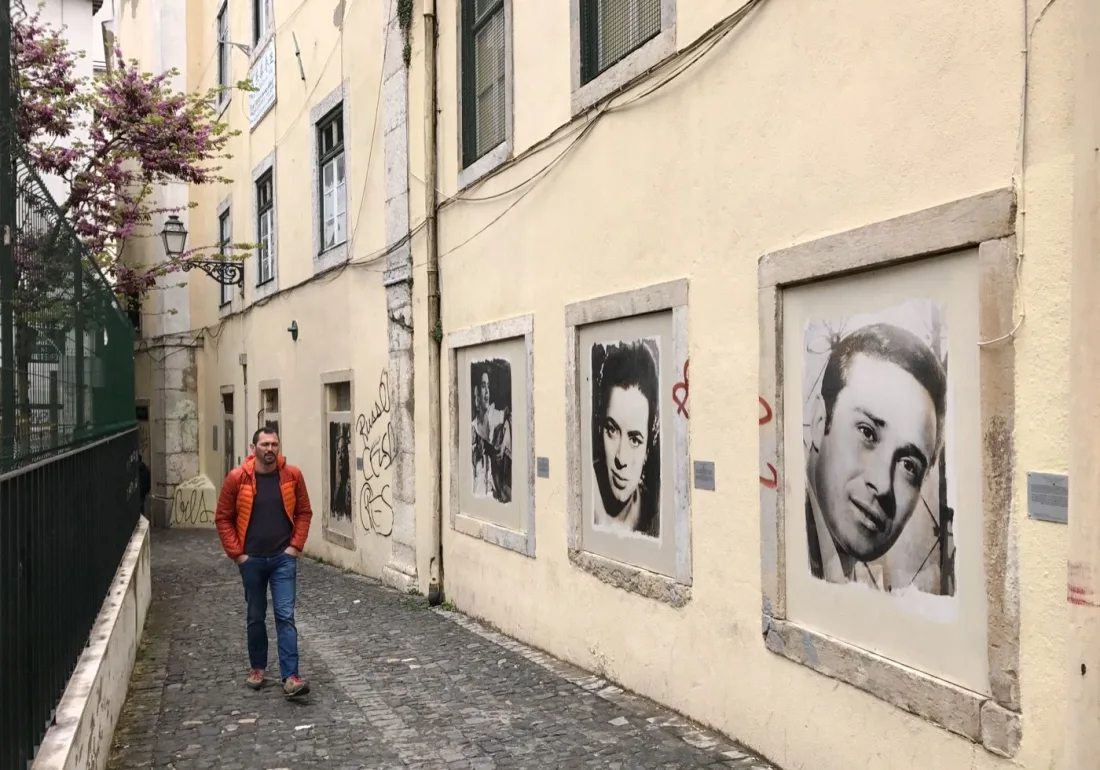 Black-and-white portraits of fado legends pasted on a wall in a Mouraria alley