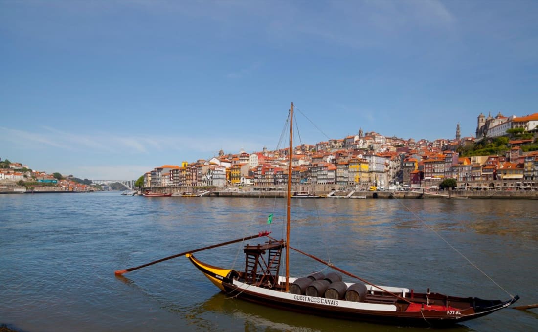 A traditional rabelo boat loaded with port wine barrels on the Douro, Porto behind