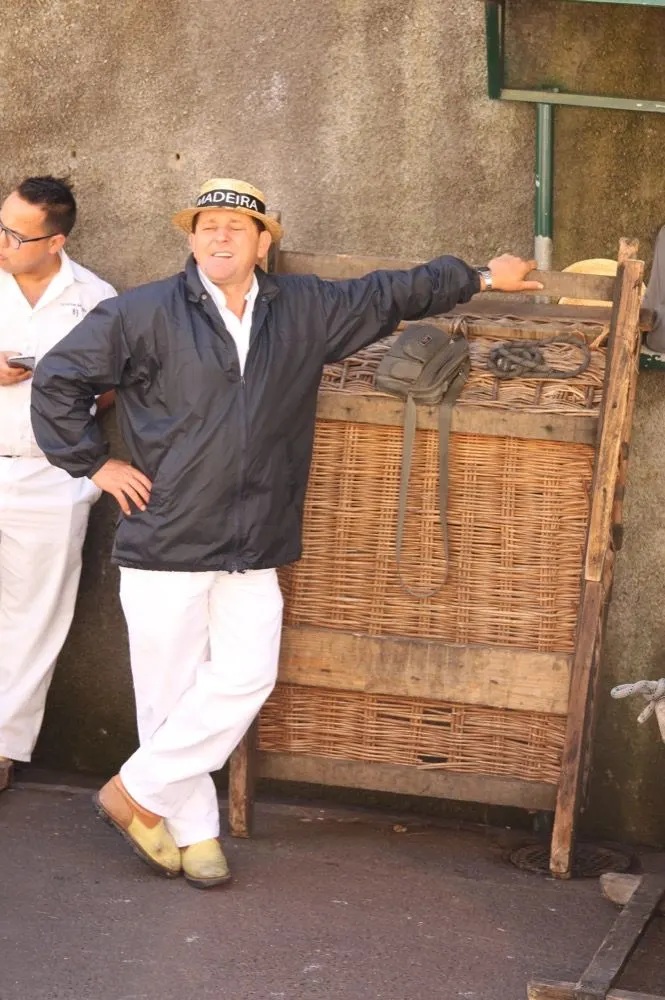 A carreiro in traditional whites beside a wicker toboggan at Monte, Funchal