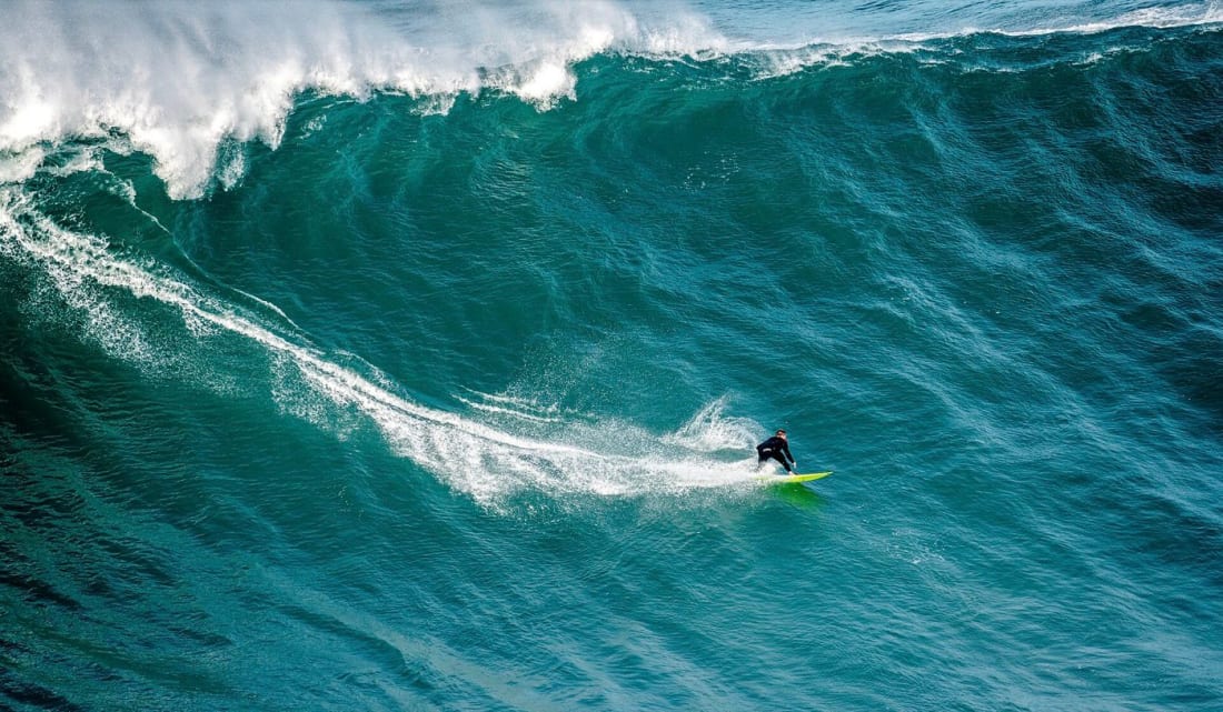 A big-wave surfer dwarfed by a turquoise wall at Praia do Norte, Nazaré