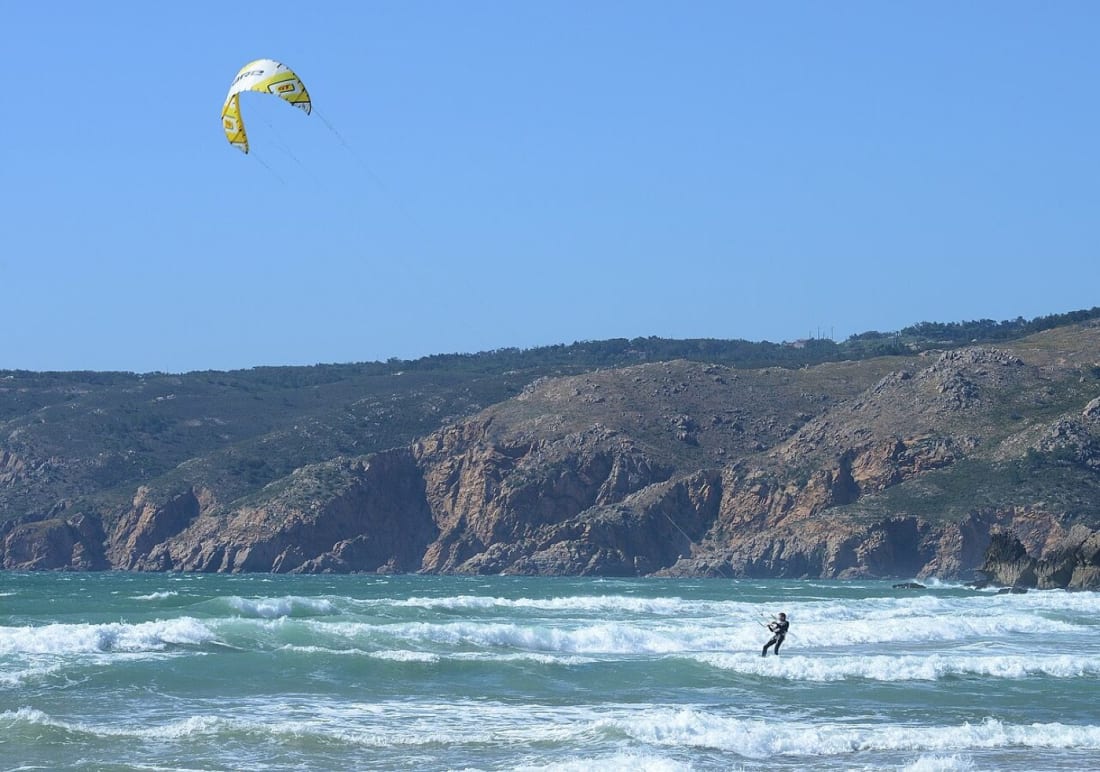 A kitesurfer riding the swell at Guincho with the Sintra hills behind