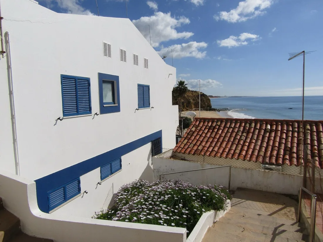 Whitewashed house with blue shutters above the beach and ochre headland at Olhos de Água, east of Albufeira