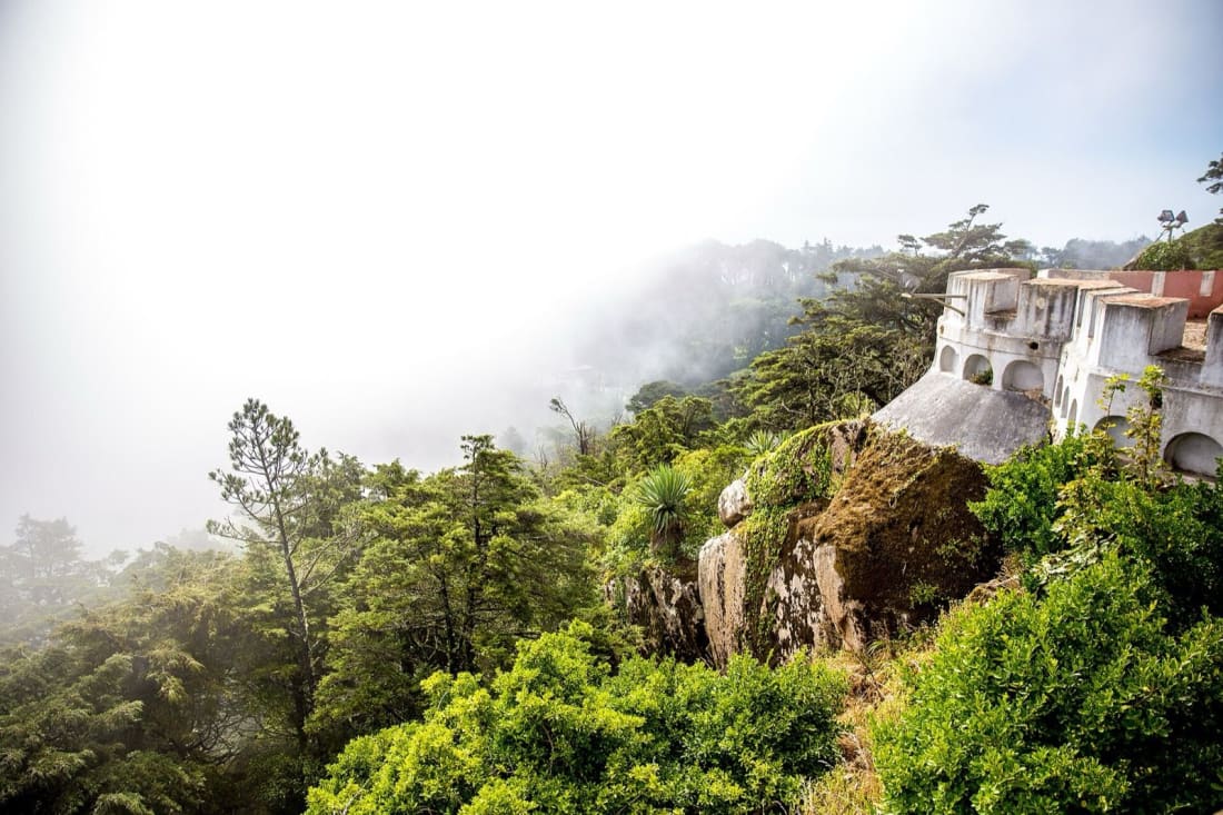 Mist rolling over the wooded ridge below the terraces of Pena Palace in Sintra